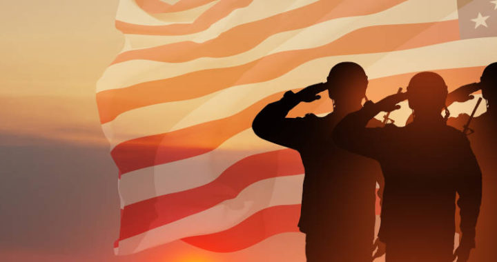 Photo montage (double exposure effect) with a silhouette of three soldiers saluting over a background that blends an American flag with a mountain sunset